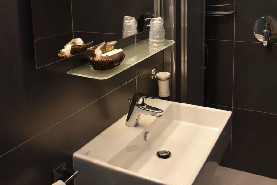 Lavabo squadrato e mensola con i prodotti cortesia, nel bagno con rivestimento scuro