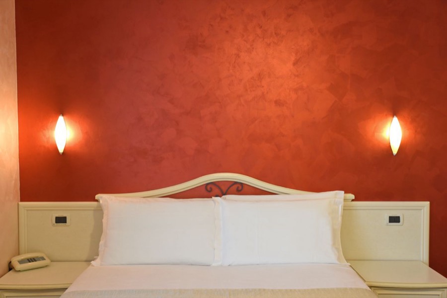 Il letto matrimoniale della Quadrupla sotto la parete rossa, con le applique accese